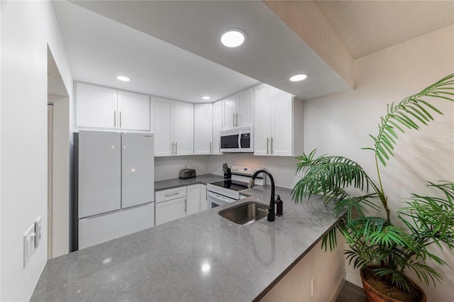 kitchen with white appliances, white cabinets, dark stone countertops, a peninsula, and a sink