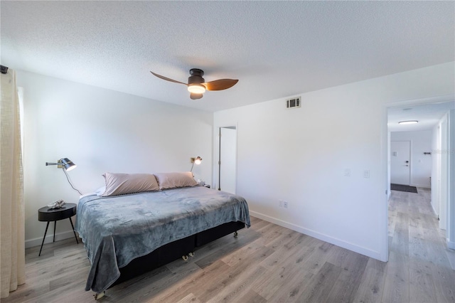 bedroom with light wood finished floors, visible vents, baseboards, a ceiling fan, and a textured ceiling