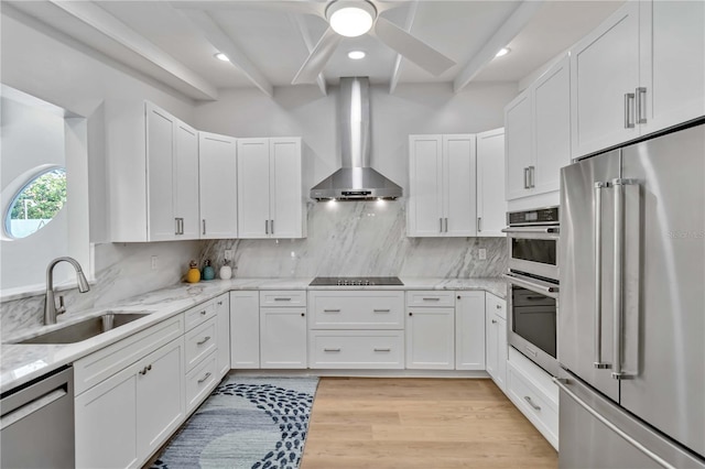 kitchen featuring appliances with stainless steel finishes, white cabinets, a sink, light stone countertops, and wall chimney exhaust hood