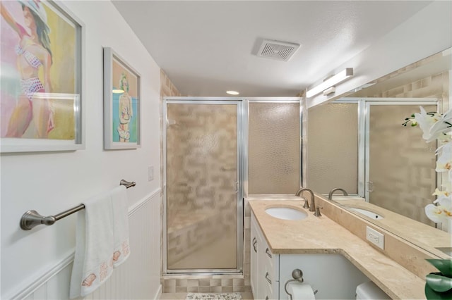 bathroom with a wainscoted wall, vanity, visible vents, and a shower stall