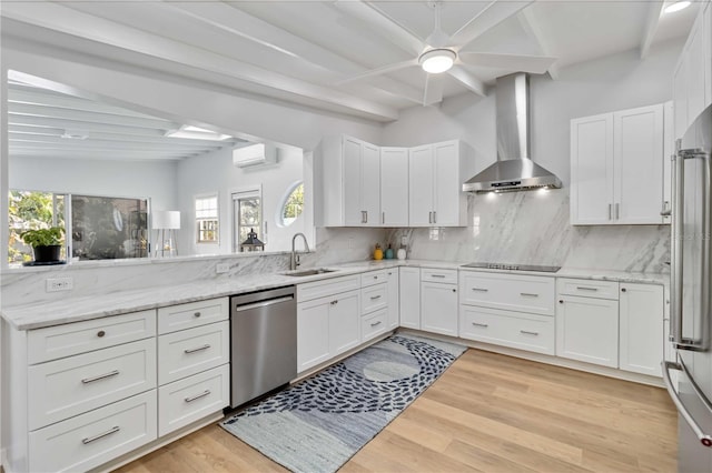 kitchen with stainless steel appliances, white cabinets, a sink, a wall mounted air conditioner, and wall chimney exhaust hood