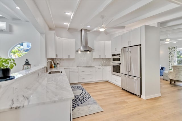 kitchen with wall chimney exhaust hood, white cabinetry, stainless steel appliances, and a sink