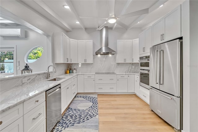 kitchen featuring a sink, white cabinets, an AC wall unit, appliances with stainless steel finishes, and wall chimney exhaust hood