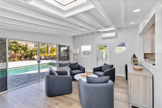 living room featuring light wood-style floors, an AC wall unit, beamed ceiling, and baseboards