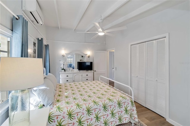 bedroom featuring light wood-style flooring, a ceiling fan, a wall mounted AC, a closet, and beamed ceiling
