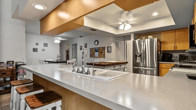 kitchen with a kitchen bar, stainless steel fridge with ice dispenser, a raised ceiling, kitchen peninsula, and ceiling fan