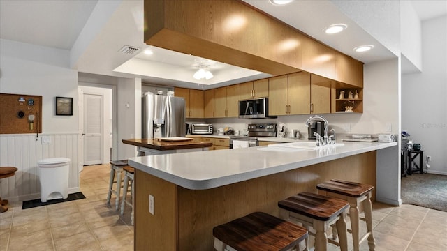 kitchen featuring kitchen peninsula, sink, a kitchen bar, a tray ceiling, and stainless steel appliances