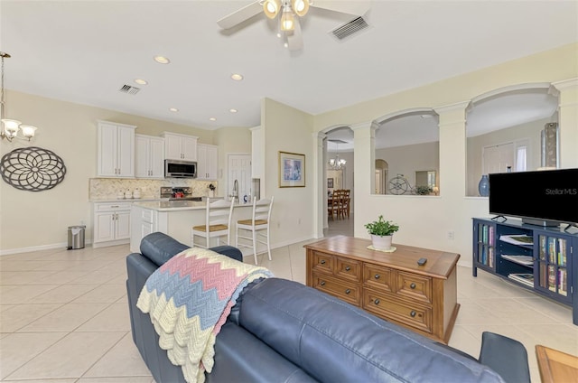 tiled living room with ceiling fan with notable chandelier and decorative columns