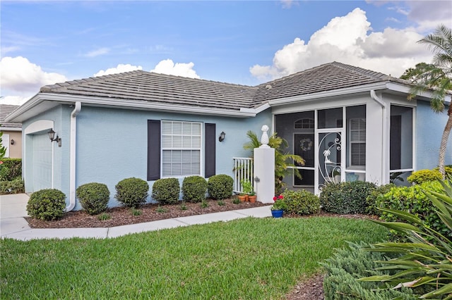 ranch-style home with stucco siding, a front yard, a sunroom, a garage, and a tiled roof