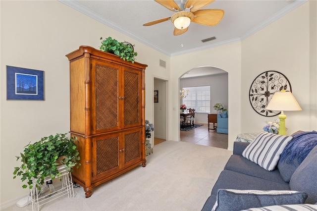 living room featuring visible vents, arched walkways, a ceiling fan, light colored carpet, and crown molding