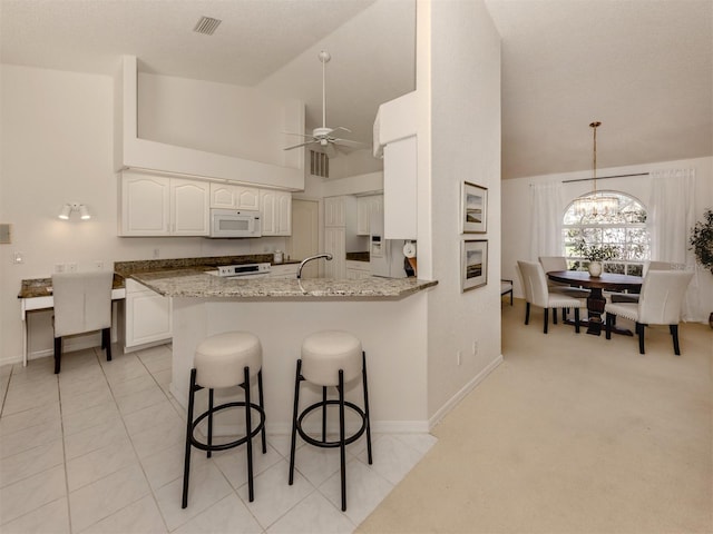 kitchen featuring a breakfast bar, white cabinetry, light stone counters, kitchen peninsula, and ceiling fan with notable chandelier