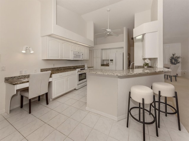 kitchen with a kitchen bar, white appliances, kitchen peninsula, ceiling fan, and white cabinets