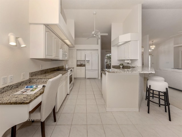 kitchen featuring a kitchen bar, white cabinetry, kitchen peninsula, stone counters, and white appliances