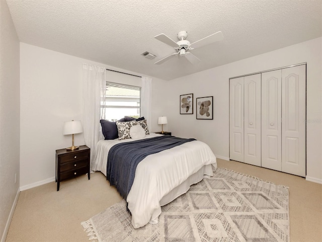 bedroom with ceiling fan, light colored carpet, a closet, and a textured ceiling