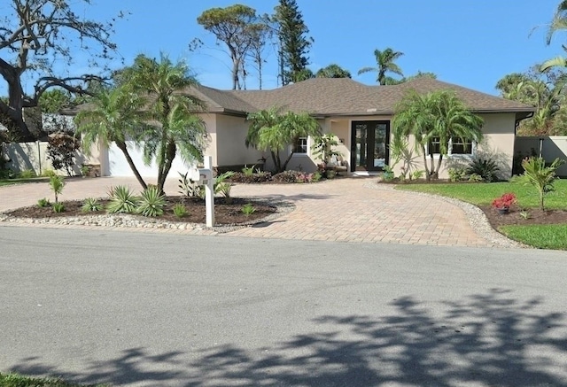 view of front of house with an attached garage, french doors, decorative driveway, and stucco siding