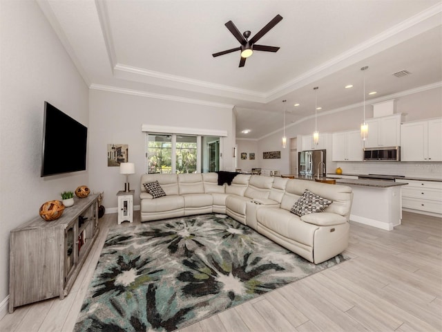 living room with a tray ceiling, crown molding, visible vents, light wood-style floors, and a ceiling fan