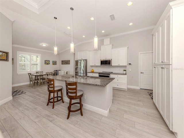 kitchen featuring stone counters, hanging light fixtures, appliances with stainless steel finishes, white cabinets, and an island with sink