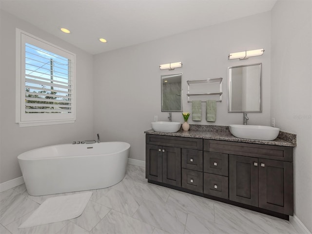 bathroom featuring a freestanding tub, baseboards, marble finish floor, and a sink