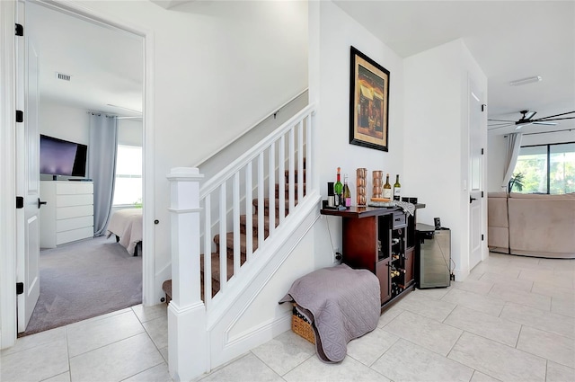 staircase featuring ceiling fan, visible vents, carpet flooring, and tile patterned floors