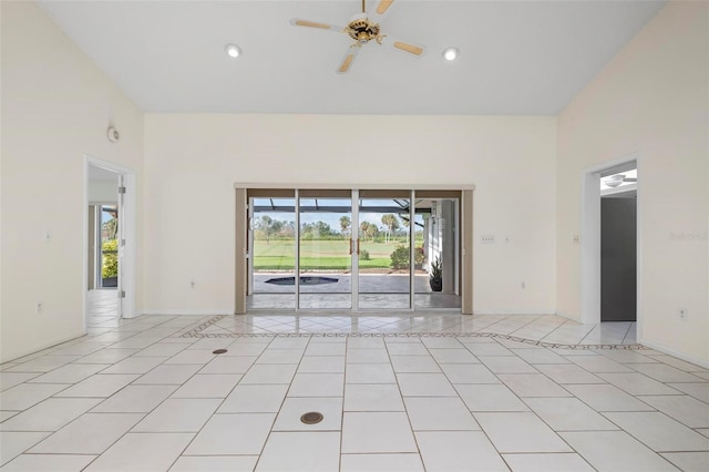 empty room with ceiling fan, a high ceiling, baseboards, and light tile patterned flooring