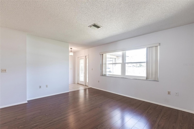 spare room featuring visible vents, a textured ceiling, baseboards, and wood finished floors