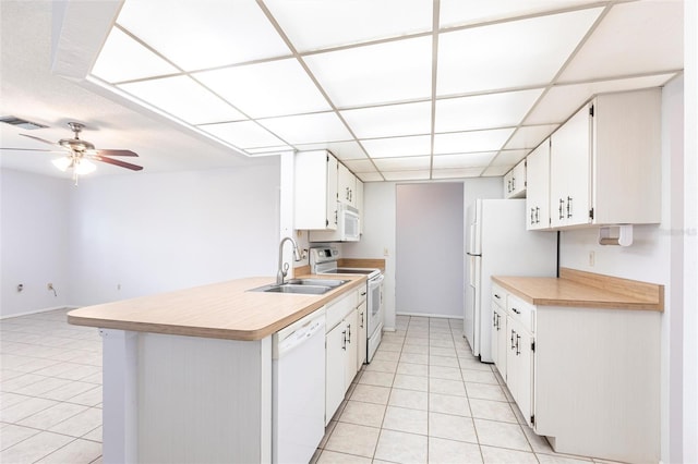 kitchen featuring a paneled ceiling, light countertops, light tile patterned flooring, a sink, and white appliances