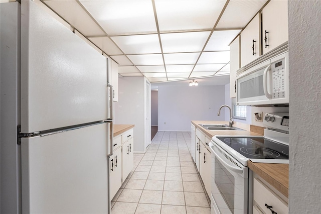 kitchen with light tile patterned flooring, a sink, white cabinetry, white appliances, and a drop ceiling