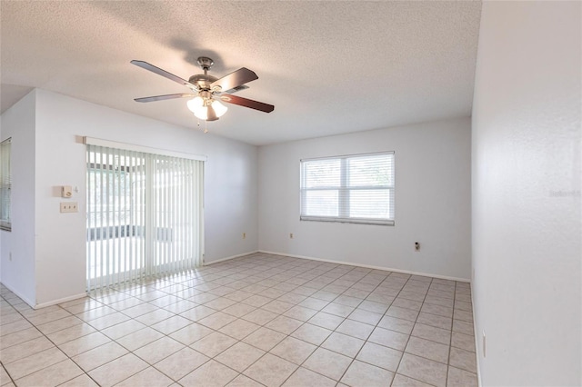 spare room with a textured ceiling, light tile patterned flooring, a ceiling fan, and baseboards