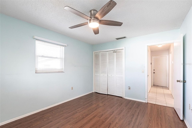 unfurnished bedroom with a closet, visible vents, a textured ceiling, and wood finished floors