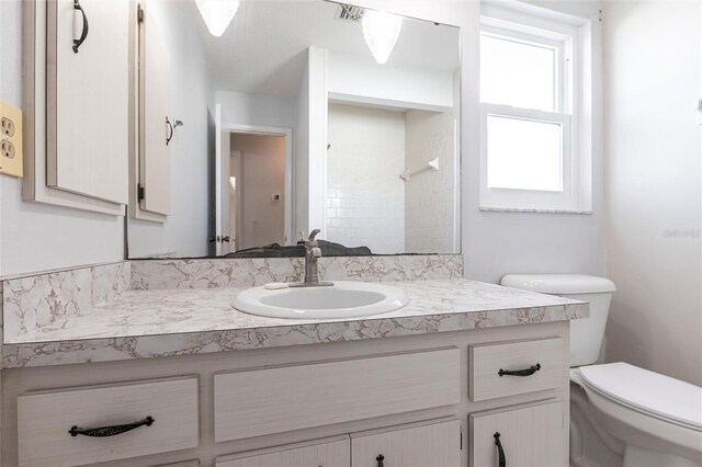 bathroom featuring tiled shower, vanity, and toilet