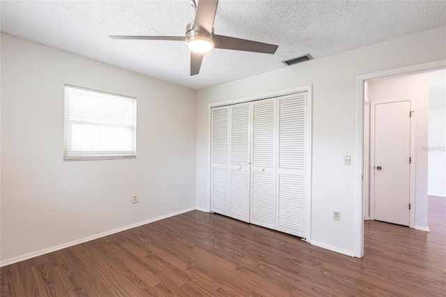 unfurnished bedroom featuring a textured ceiling, wood finished floors, visible vents, baseboards, and a closet