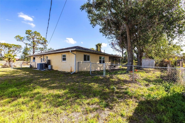 exterior space with a fenced backyard, an outbuilding, a yard, central air condition unit, and stucco siding