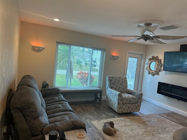 living area with a glass covered fireplace, dark wood-style flooring, visible vents, and baseboards