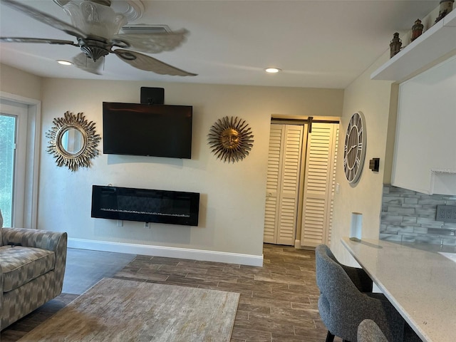 living area featuring recessed lighting, a glass covered fireplace, a ceiling fan, and baseboards