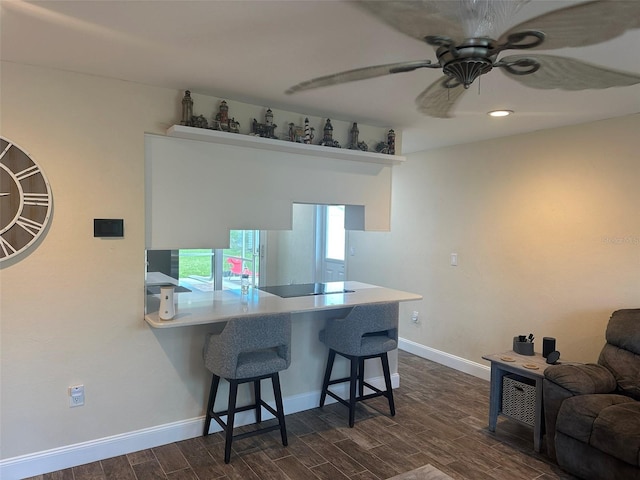 kitchen featuring a breakfast bar, dark wood-style flooring, light countertops, a peninsula, and baseboards