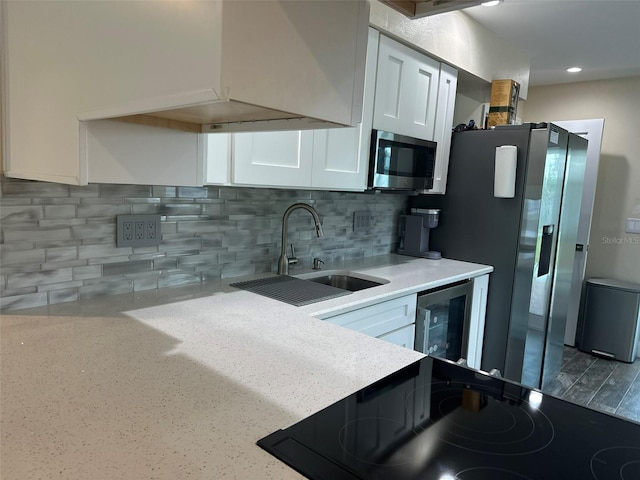 kitchen with beverage cooler, appliances with stainless steel finishes, light countertops, white cabinetry, and a sink