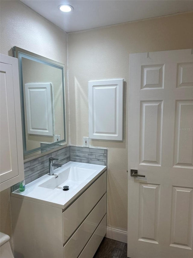 bathroom with tasteful backsplash, vanity, baseboards, and wood finished floors