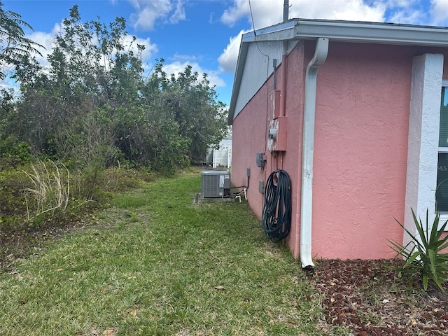 view of side of property featuring a yard, stucco siding, and central air condition unit