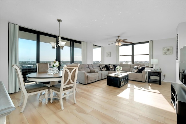 living room featuring a wall of windows, ceiling fan with notable chandelier, and light hardwood / wood-style flooring