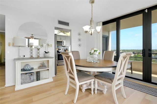 dining area featuring ceiling fan with notable chandelier, a wealth of natural light, and light wood-type flooring