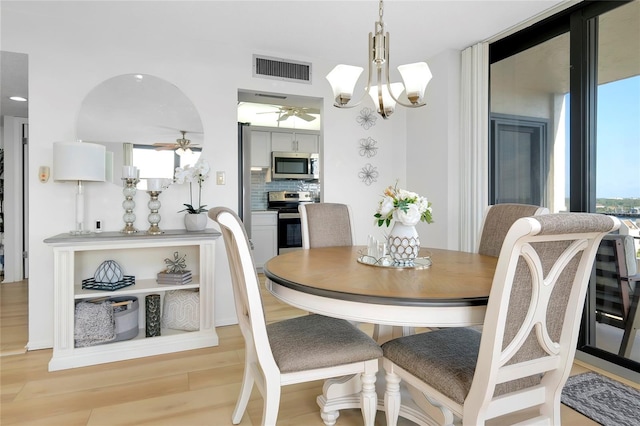 dining area with ceiling fan with notable chandelier, a wealth of natural light, and light wood-type flooring