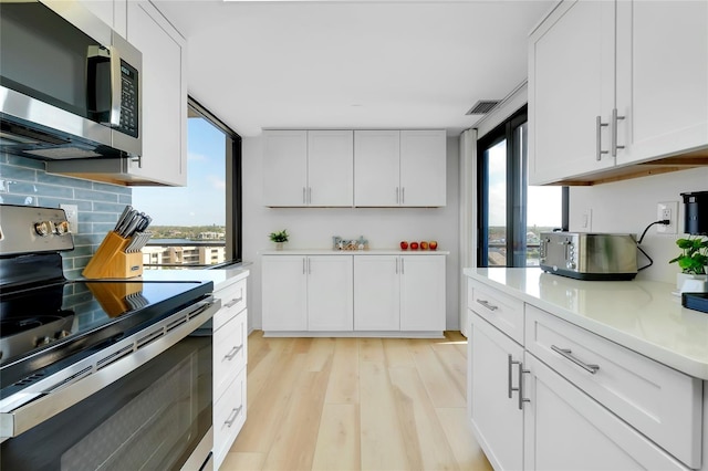 kitchen featuring stainless steel appliances, white cabinetry, a wealth of natural light, and light wood-type flooring