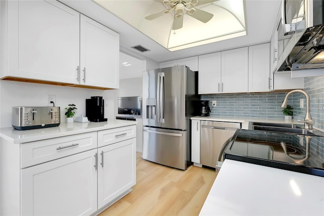 kitchen with sink, white cabinetry, light wood-type flooring, appliances with stainless steel finishes, and backsplash