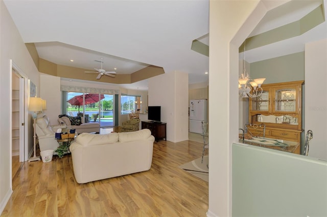 living room featuring ceiling fan with notable chandelier and light wood-type flooring