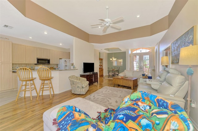 living room with ceiling fan with notable chandelier, light hardwood / wood-style floors, and french doors