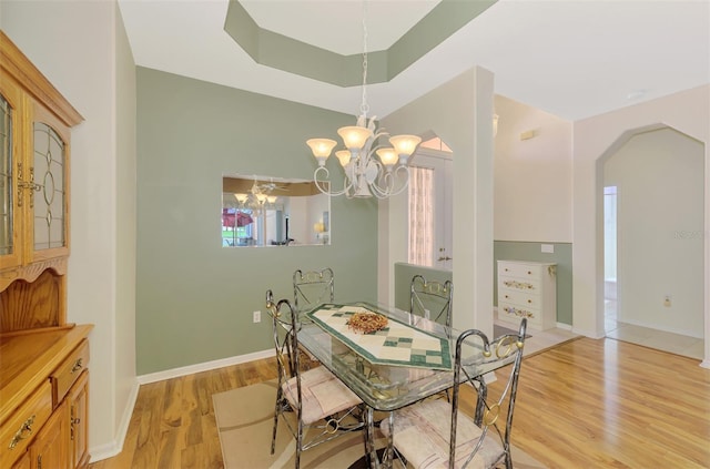 dining room featuring a tray ceiling, a chandelier, and light hardwood / wood-style flooring