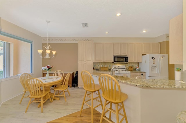 kitchen with backsplash, hanging light fixtures, white appliances, light stone counters, and an inviting chandelier