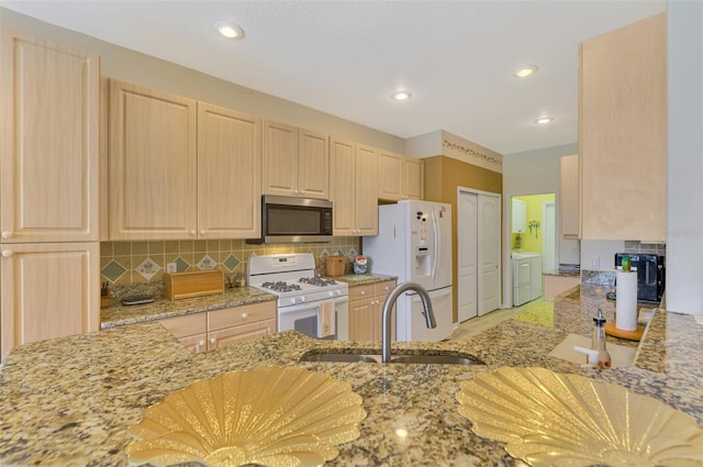 kitchen with sink, white appliances, light stone counters, separate washer and dryer, and light brown cabinets