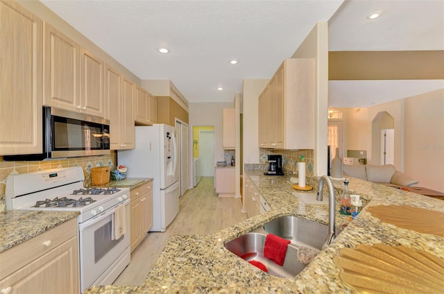 kitchen with sink, white appliances, light stone counters, light brown cabinetry, and kitchen peninsula