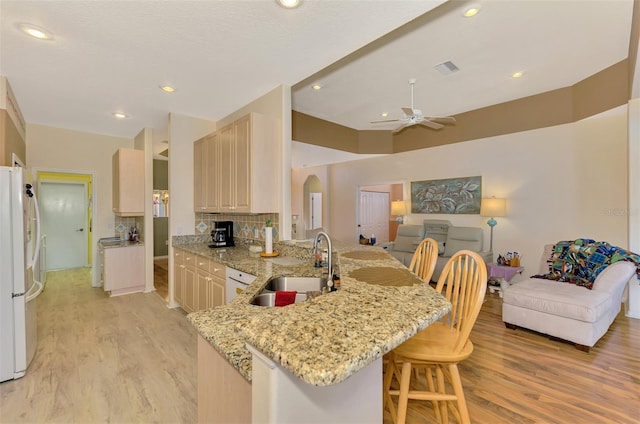 kitchen with sink, a kitchen bar, white refrigerator, light stone counters, and kitchen peninsula